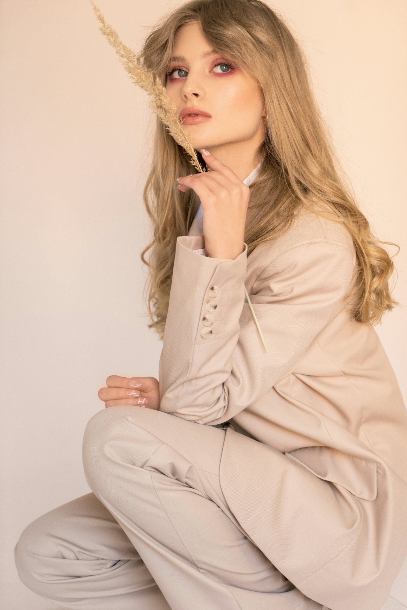 Modelo sentada com conjunto de alfaiataria rosé, segurando um ramo seco